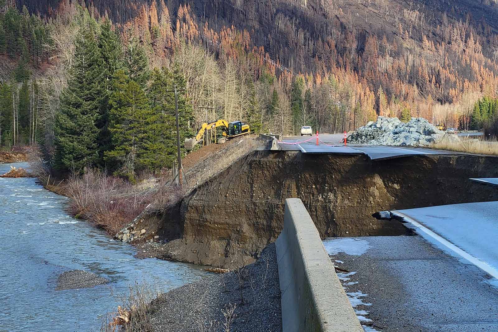 Highway with a piece of road missing due to the erosion of the ground under. A river is under and beside the road.
